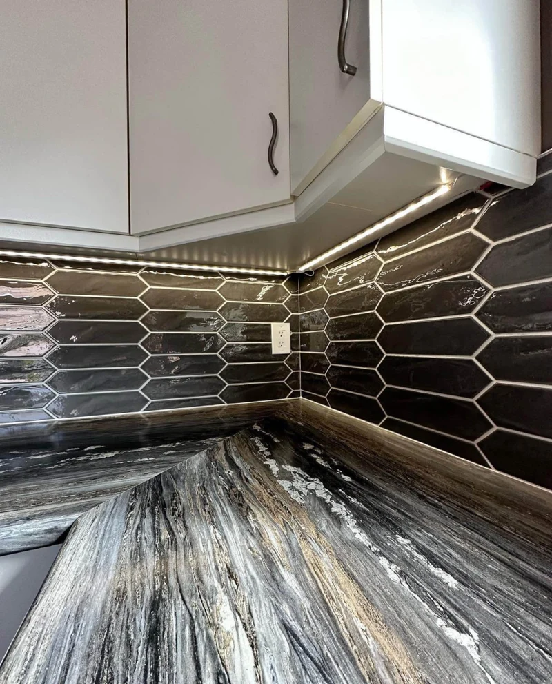 Dark elongated tile backsplash with light grout below white kitchen cabinets