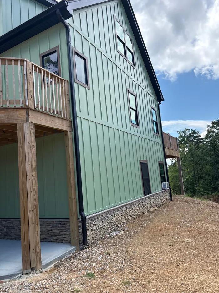Green board-and-batten exterior with windows, wood trim and stone lower wall