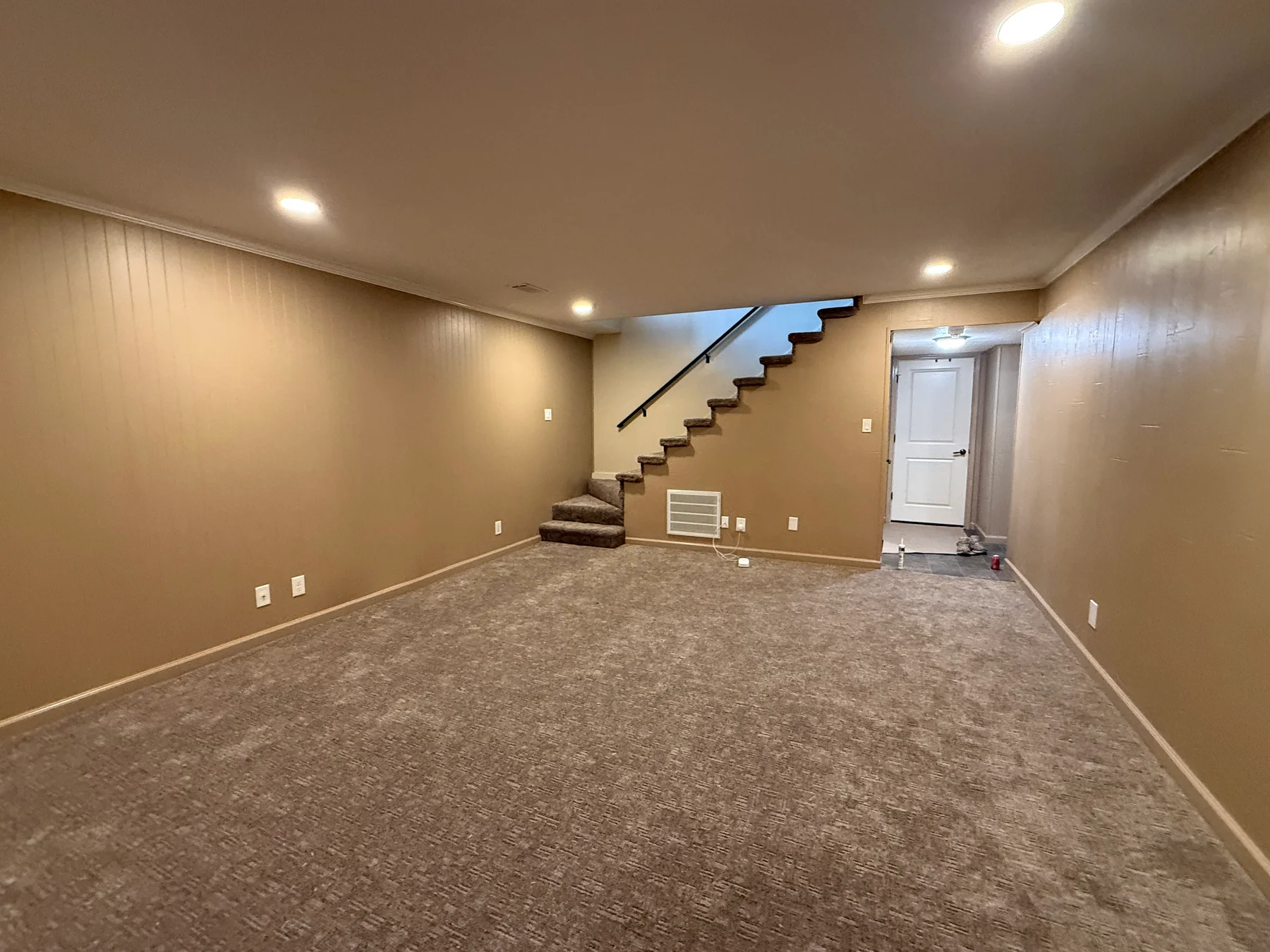 Remodeled basement living area with gray carpet, painted walls, recessed lights and stairs