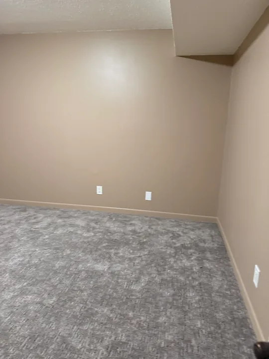 Finished basement room corner with gray carpet and painted walls