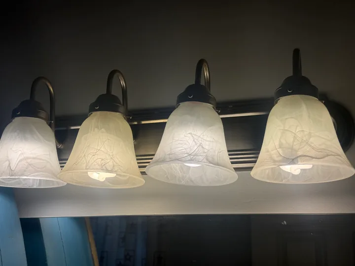 Row of four bathroom vanity lights above a mirror