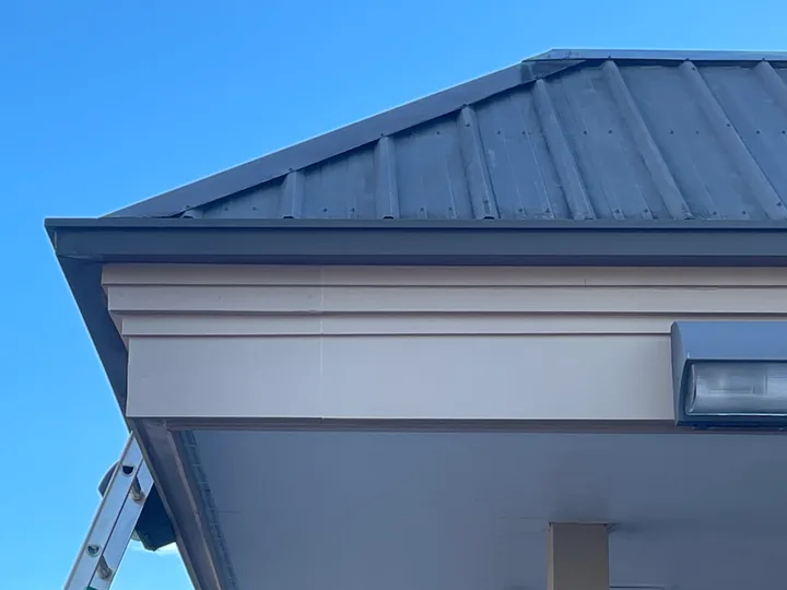 Commercial canopy, metal roof edge and fascia beneath a clear blue sky