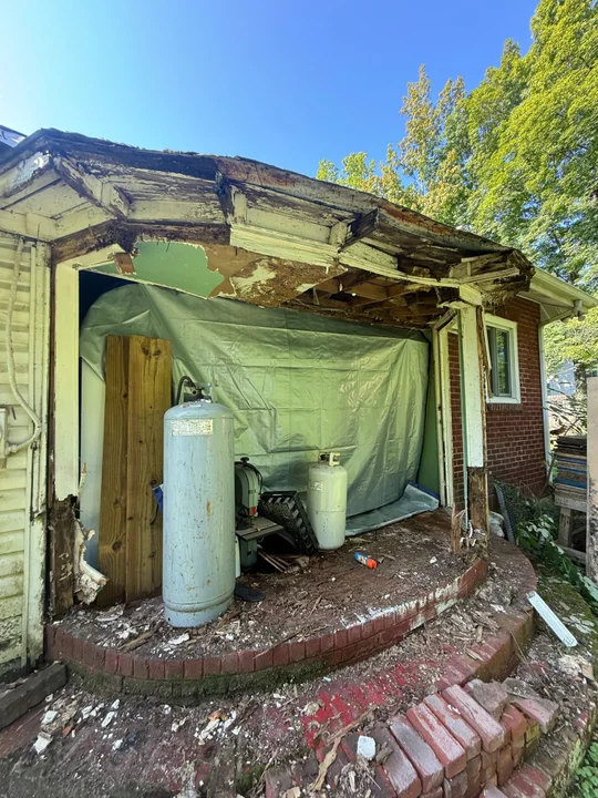 Deteriorated entry trim, exposed roof framing and an open wall above the curved brick steps