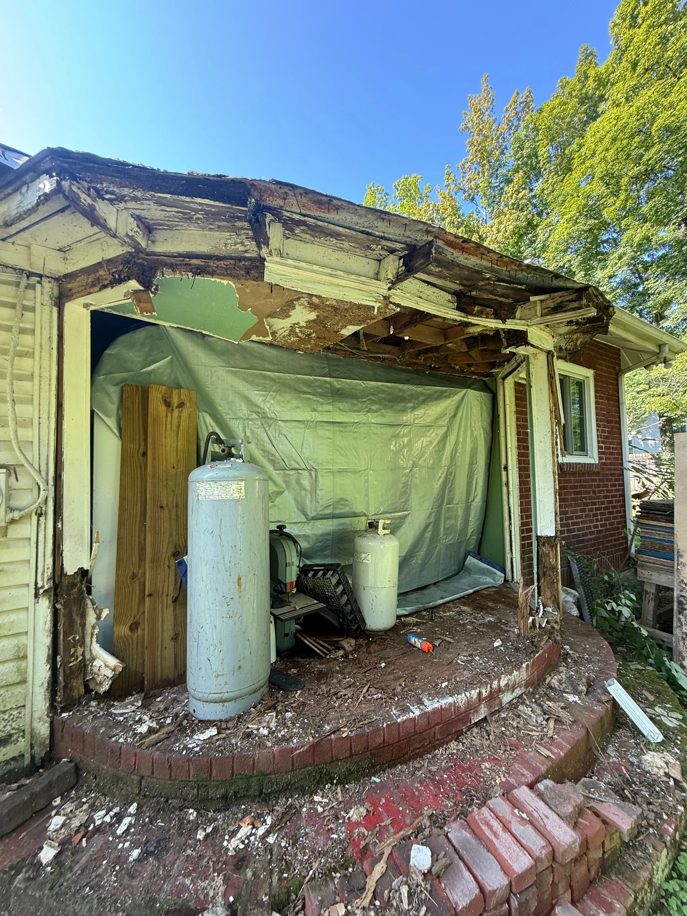 Deteriorated entry trim, exposed roof framing and an open wall above the curved brick steps