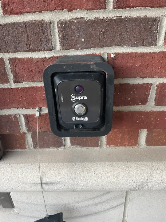 Supra key lockbox mounted on exterior brick beside trim