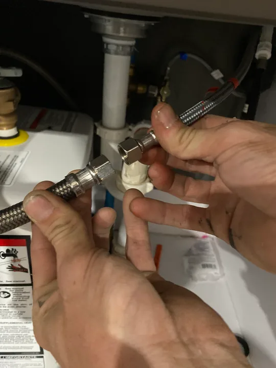 Hands working on a plumbing connection below a fixture