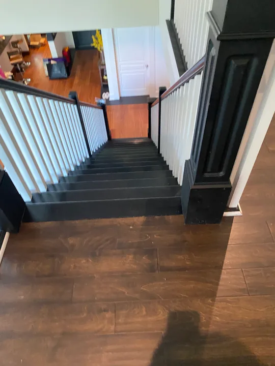 Wood-grain flooring meeting a staircase and dark stair balusters
