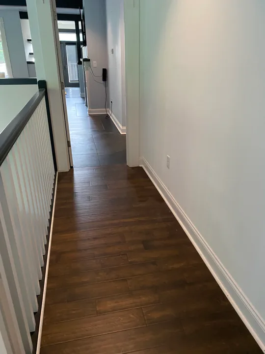 Wood-grain flooring meeting a staircase and dark stair balusters