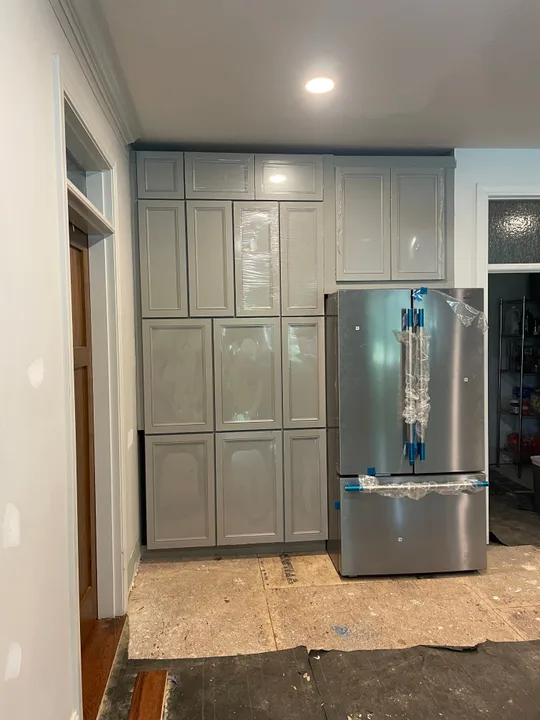 Tall gray kitchen cabinets and a stainless refrigerator during installation