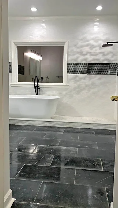 Gray tiled bathroom with glass shower enclosure and white vanity