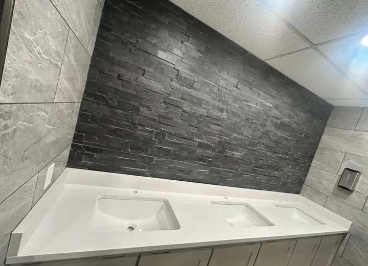 Gray tiled bathroom with glass shower enclosure and white vanity