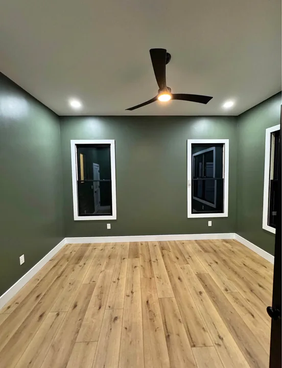 Light wood flooring in a green room with dark window trim