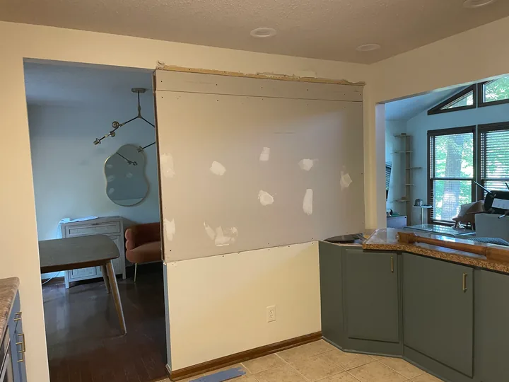 Kitchen wall with drywall patches and joint compound beside cabinets