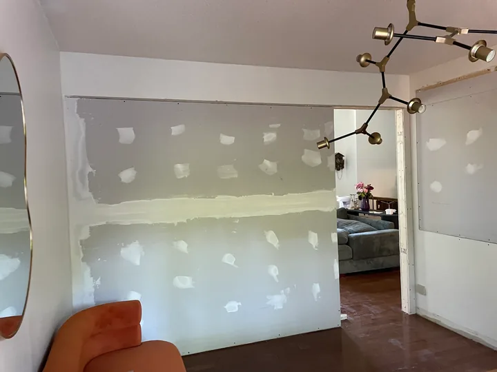 Kitchen wall with drywall patches and joint compound beside cabinets