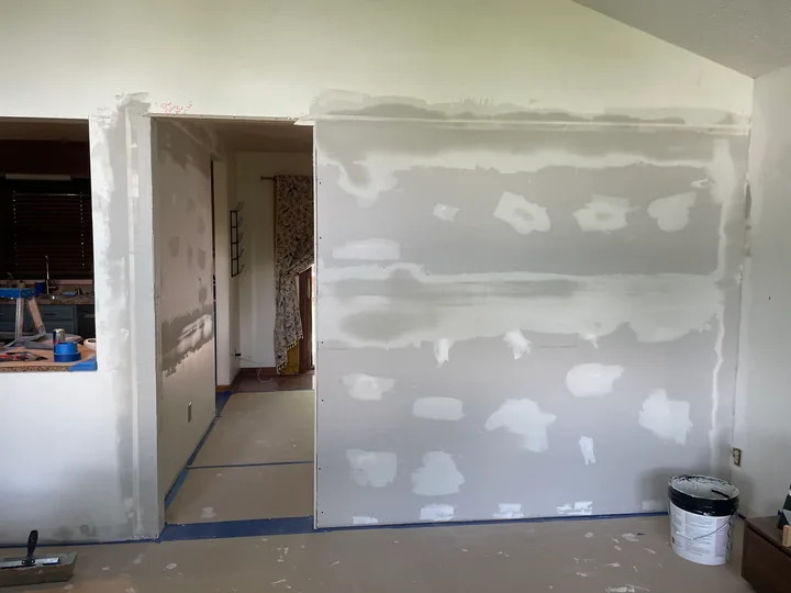 Kitchen wall with drywall patches and joint compound beside cabinets