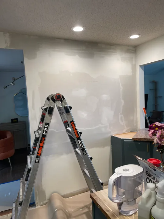 Kitchen wall with drywall patches and joint compound beside cabinets