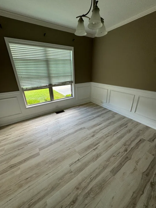 Light plank flooring beside white wall paneling and baseboards