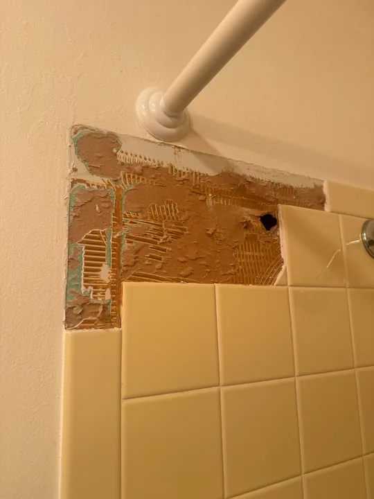 Tile removed around a shower fitting with backing exposed