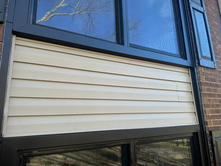 Siding panels and dark window frames on a brick building