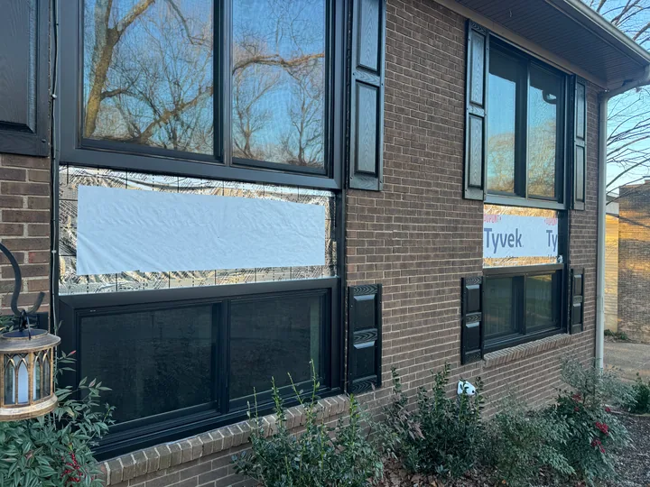 Siding panels and dark window frames on a brick building
