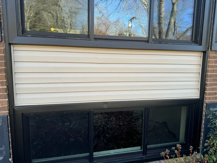 Siding panels and dark window frames on a brick building
