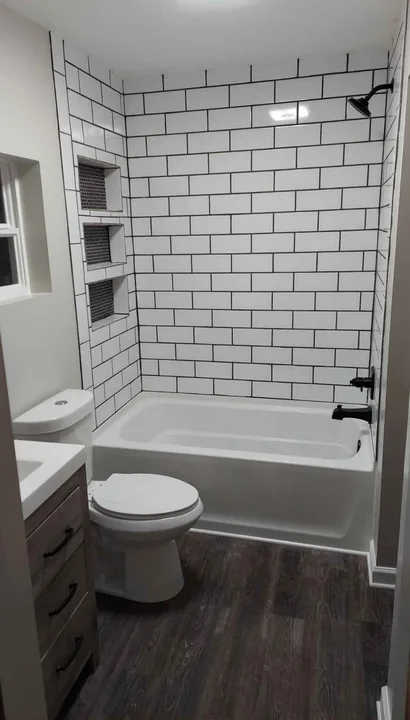 Compact bathroom with white vanity, toilet and tiled tub surround