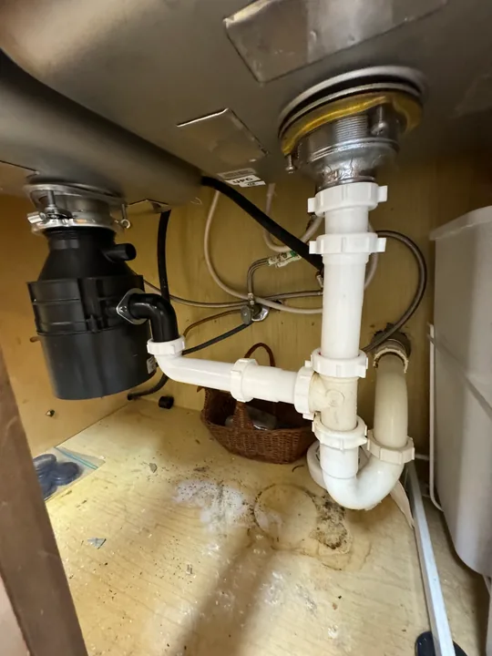 Kitchen sink drain, disposal and plumbing connections beneath a counter