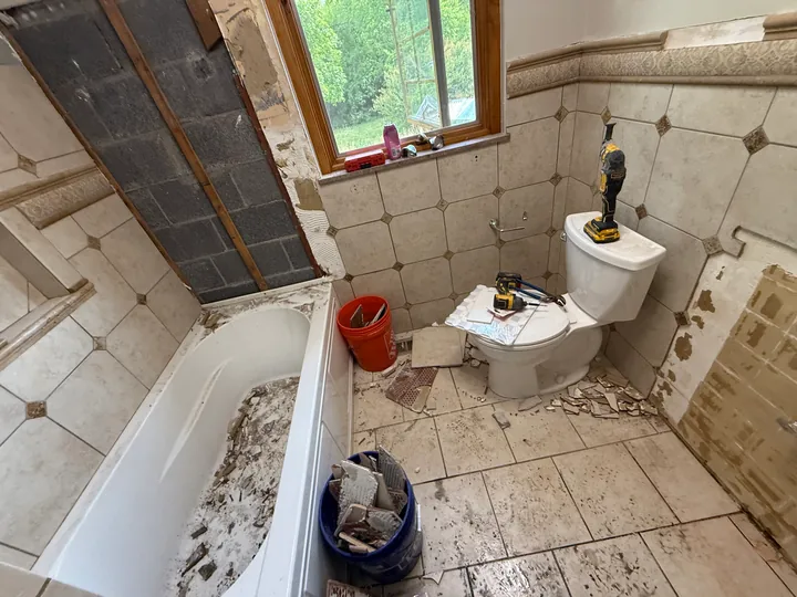 Bathroom during demolition with opened surfaces beside the wood-framed window