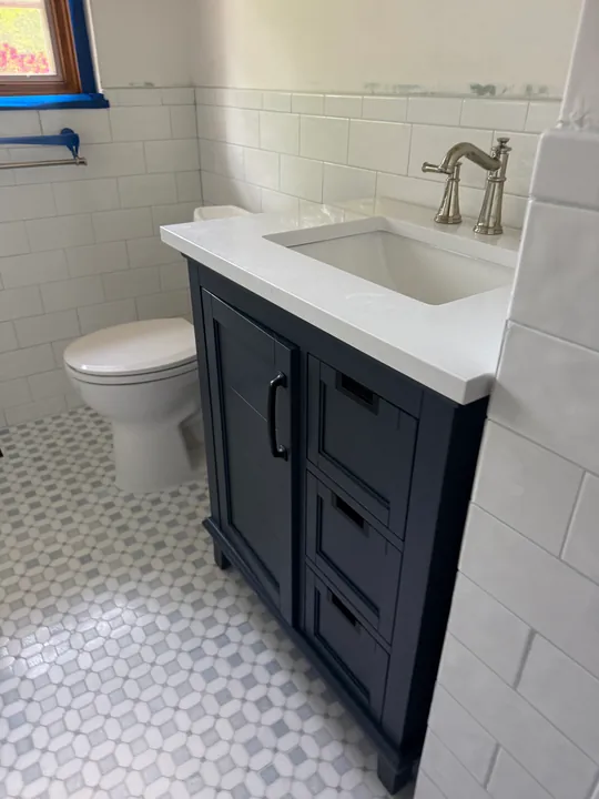 Dark bathroom vanity, toilet and mosaic floor with white wall tile