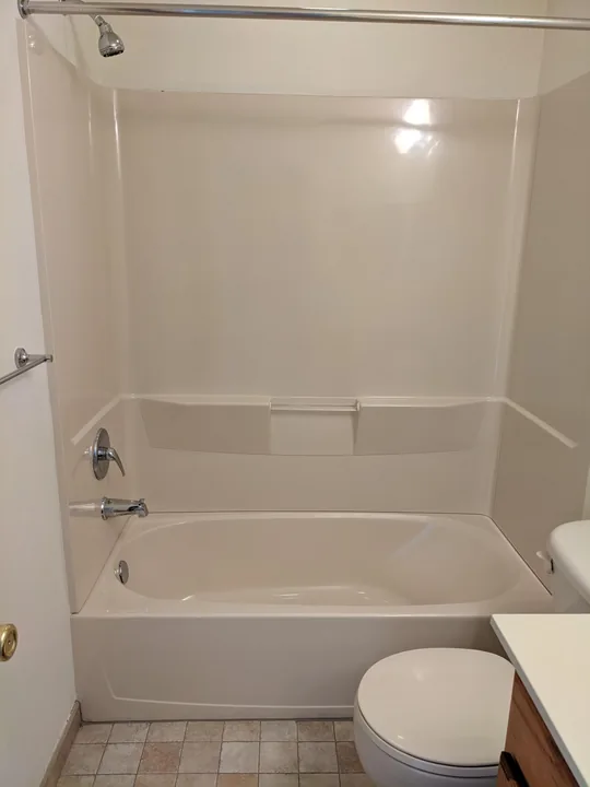 White tub and surround beside a bathroom vanity and toilet