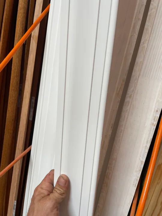 A hand holding white trim beside an unfinished window opening